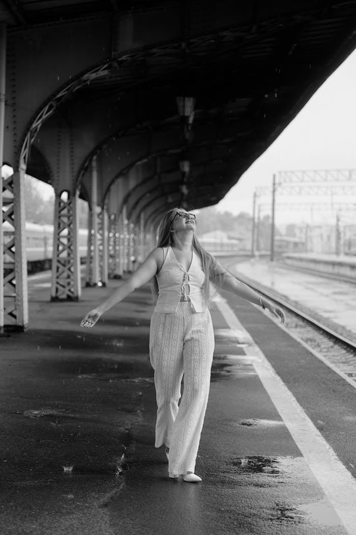 Happy woman enjoying rain at a train station, embracing the moment.