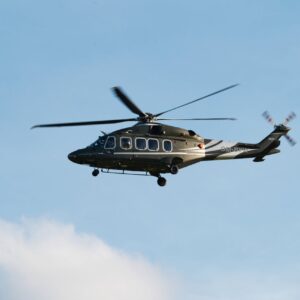 A medium-sized helicopter in flight over Poprad, Slovakia, against a clear blue sky.