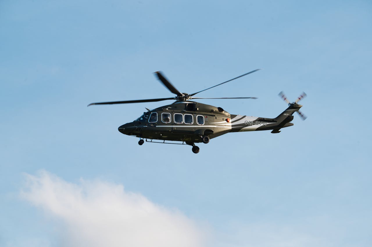 A medium-sized helicopter in flight over Poprad, Slovakia, against a clear blue sky.