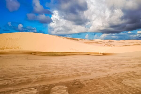 Explore the vast sand dunes of Maranhão, Brazil, set against a backdrop of dramatic, cloudy skies.