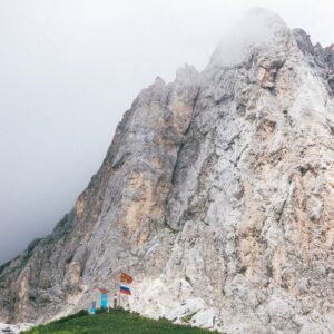 Scenic view of a misty alpine landscape featuring a rugged rocky mountain peak and lush greenery.