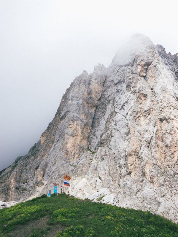 Scenic view of a misty alpine landscape featuring a rugged rocky mountain peak and lush greenery.